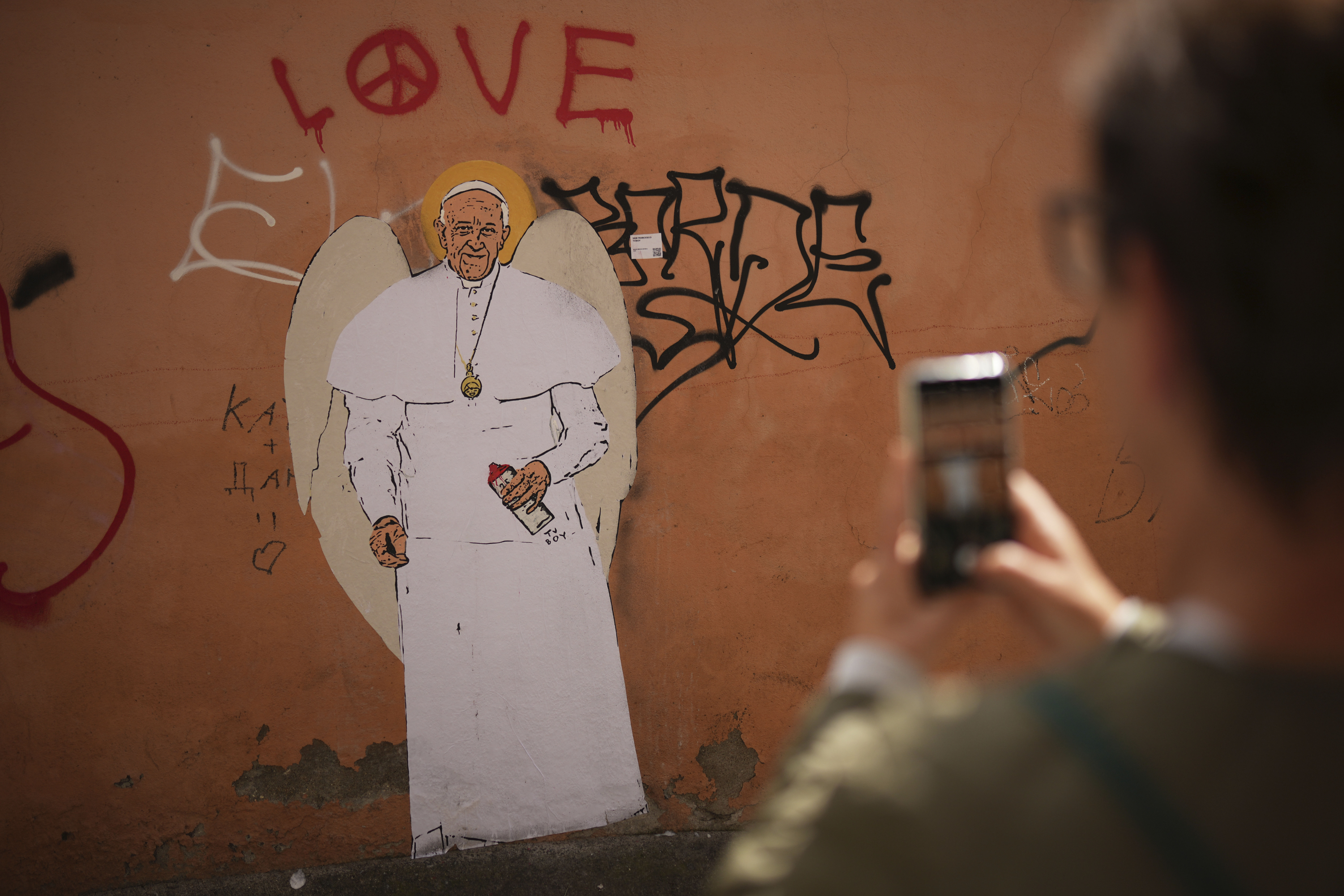 A person takes a picture of a graffiti mural of Pope Francis, near the Vatican, Friday, April 25, 2025. (AP Photo/Francisco Seco)