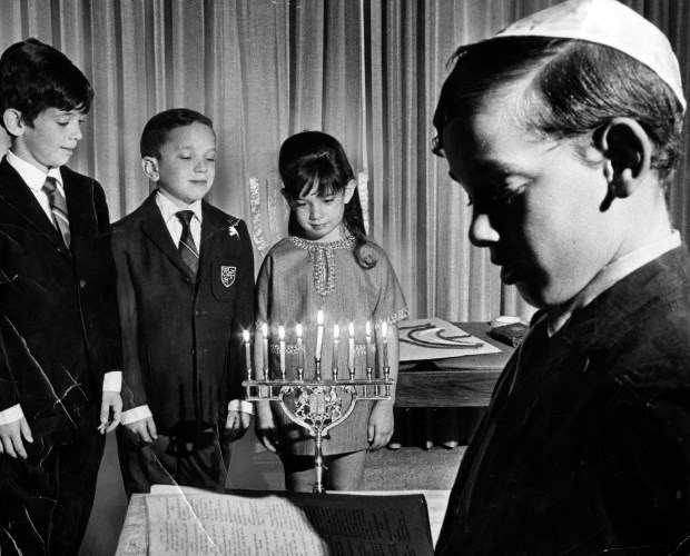 Children of the Paley family in Skokie mark the beginning of Hanukkah in December, 1969. Mark, 8, left, Howard, 7, and Leah, 5, stand before the menorah while the oldest, Norman, 9, reads from the prayer book. (Steve Lasker/Chicago Today)